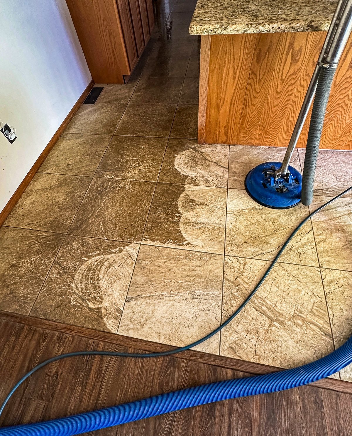 A professional floor cleaning machine in action, effectively removing dirt and grime from a tiled kitchen floor. The difference between the cleaned and uncleaned sections is clearly visible, showcasing the machine's powerful cleaning capabilities.